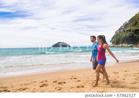 New Zealand beach couple hikers walking the coast track in Abel Tasman National Park. People tramping relaxing in nature outdoors. 67982527
