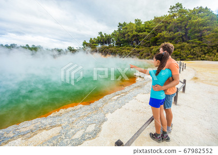 New Zealand travel tourists couple at Champagne pool at Wai-O-Tapu pools Sacred Waters. Tourist attraction in Waiotapu, Rotorua, north island. Active geothermal area, Okataina Volcanic Centre, Taupo. 67982552