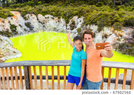 New Zealand tourist attraction couple tourists taking selfie travel destination, Waiotapu. Active geothermal green pond, Rotorua, north island, Wai-O-Tapu, New Zealand. 67982568