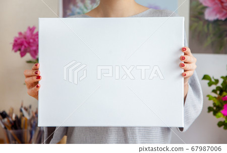 Smiling young woman artist is holding a blank white canvas Smiling young woman artist is holding a blank white canvas 67987006