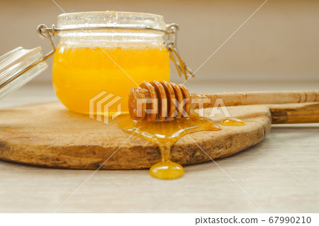 Honey dripping from a wooden dipper and glass jar 67990210