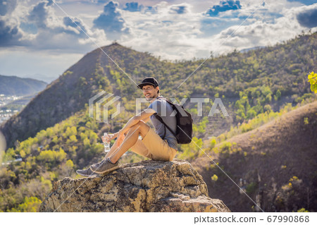 A young man local tourist sits on a rock and enjoys the view of her city. Local tourism concept. Tourism after COVID 19 67990868