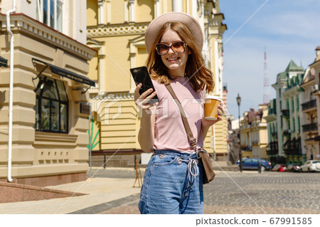 Beautiful Young Woman tourist with takeout coffee in the City Center talking on the phone Beautiful Young Woman tourist with takeout coffee in the City Center talking on the phone 67991585