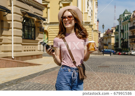 Beautiful Young Woman tourist with takeout coffee in the City Center talking on the phone Beautiful Young Woman tourist with takeout coffee in the City Center talking on the phone 67991586