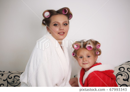 Mom and baby girl are in bathrobes and curlers on her head. 67993343