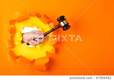 Hand holding a judge's gavel through torn orange Hand holding a judge's gavel through torn orange 67994482