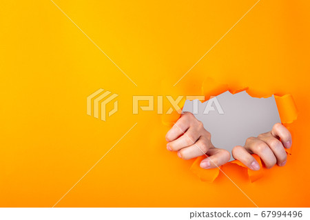 Hands ripping a hole in orange paper Hands ripping a hole in orange paper 67994496
