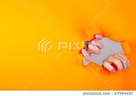 Hands ripping a hole in orange paper Hands ripping a hole in orange paper 67994497
