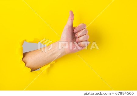 Hand showing a thumb up sign through a ripped hole Hand showing a thumb up sign through a ripped hole 67994500