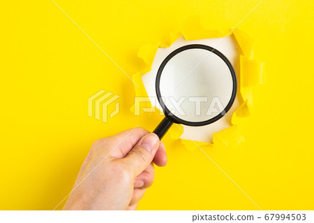 A human hand holds a magnifying glass through a 67994503