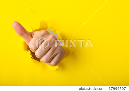 Hand showing a thumb up sign through a ripped hole Hand showing a thumb up sign through a ripped hole 67994507