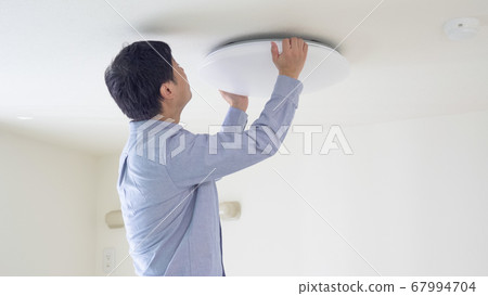 一個男人把吸頂燈放到天花板上 67994704