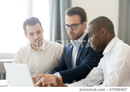 Diverse interns listening to mentor pointing at laptop screen Diverse interns listening to mentor pointing at laptop screen 67996987