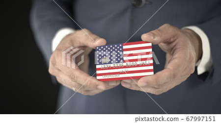 Businessman holding plastic bank card with printed flag of the United States, fictional numbers Businessman holding plastic bank card with printed flag of the United States, fictional numbers 67997151