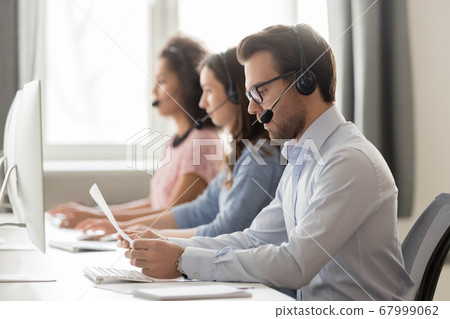 Serious call center agent in headset reading paper documents 67999062