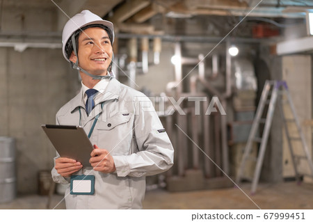 A smiling director wearing a helmet and checking the site while looking at the tablet 67999451