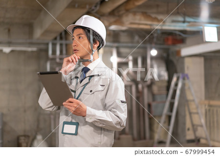 A director wearing a helmet and checking the site while looking at the tablet 67999454