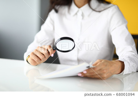 Woman sits at table and holds magnifying glass and documents in her hands. Woman sits at table and holds magnifying glass and documents in her hands. 68001094