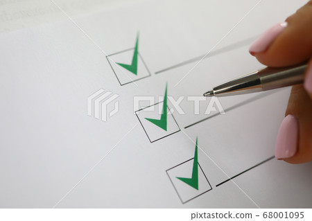 Woman's hand holds pen and marks green check marks in document. 68001095