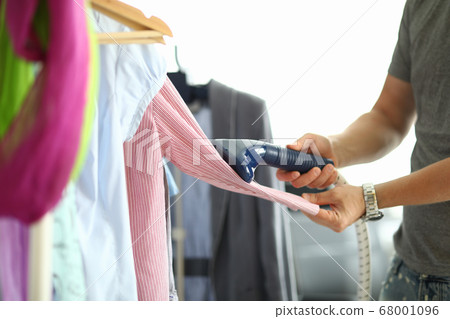 Man holds steamer in his hands and ironing shirt on hanger Man holds steamer in his hands and ironing shirt on hanger 68001096