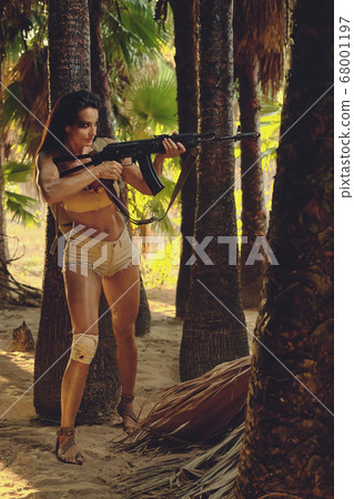 Athletic woman holding gun posing in palm trees Athletic woman holding gun posing in palm trees 68001197