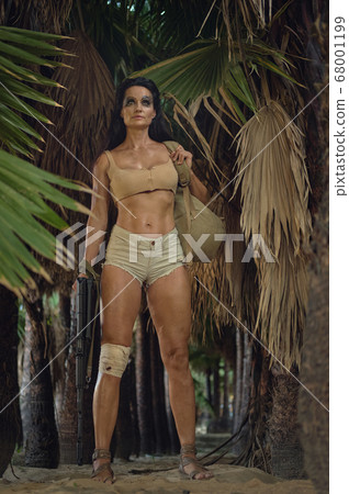 Athletic woman holding gun posing in palm trees Athletic woman holding gun posing in palm trees 68001199