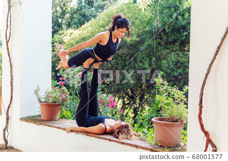 Two beautiful women doing acroyoga in the garden or park Two beautiful women doing acroyoga in the garden or park 68001577
