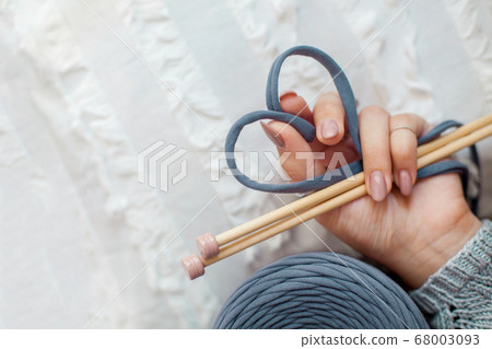 A woman's hand holds a blue knitted yarn, folding it in the shape of a heart. Concept of love for knitting and handicraft. 68003093