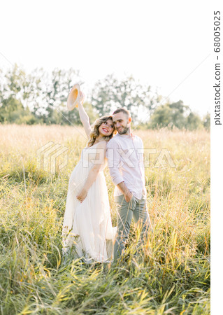 Family, motherhood and pregnancy concept. Happy couple waiting for a baby in sunny day, standing back to back in the field Family, motherhood and pregnancy concept. Happy couple waiting for a baby in sunny day, standing back to back in the field 68005025