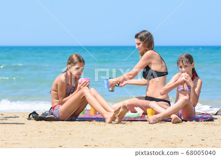 Children and mom eat while sitting on the seashore Children and mom eat while sitting on the seashore 68005040