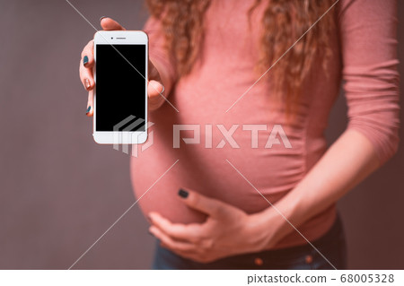 Pregnant woman with smartphone, showing mobile phone with empty blank screen. Smartphone mockup 68005328