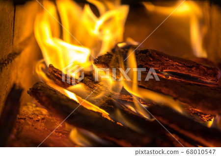 Flame incinerates firewood and transforms it ashes, close up, shallow depth of field. Blaze in a large stove. Nature texture of fire. The flame of fire burns in the brazier, smoldering firewoods. 68010547