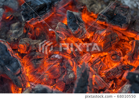 Flame incinerates firewood and transforms it ashes, close up, shallow depth of field. Blaze in a large stove. Nature texture of fire. The flame of fire burns in the brazier, smoldering firewoods. 68010550
