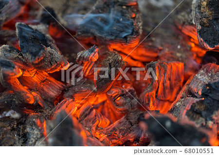 Flame incinerates firewood and transforms it ashes, close up, shallow depth of field. Blaze in a large stove. Nature texture of fire. The flame of fire burns in the brazier, smoldering firewoods. 68010551