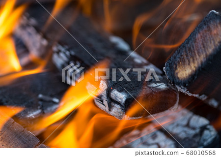 Flame incinerates firewood and transforms it ashes, close up, shallow depth of field. Blaze in a large stove. Nature texture of fire. The flame of fire burns in the brazier, smoldering firewoods. 68010568