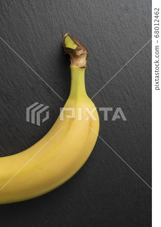 Ripe unpeeled banana with bright yellow peel on a stone surface. Gray textured board. Tropical ingredients concept 68012462