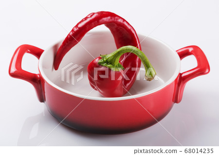 red bent pepper lies in a red saucepan, on a white red bent pepper lies in a red saucepan, on a white 68014235