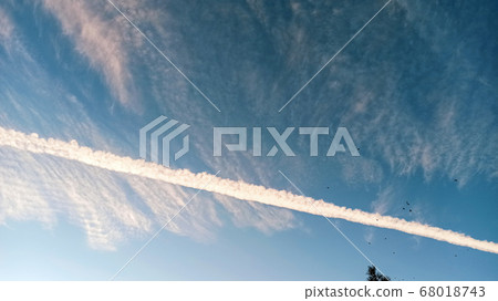 Pattern of airplane trails cutting blue sky in half. Airplane leaving behind a long white trail at the clear blue sky. Pattern of airplane trails cutting blue sky in half. Airplane leaving behind a long white trail at the clear blue sky. 68018743