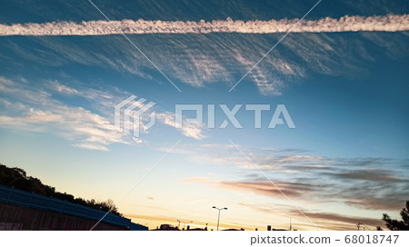 Pattern of airplane trails cutting blue sky in half. Airplane leaving behind a long white trail at the clear blue sky. 68018747