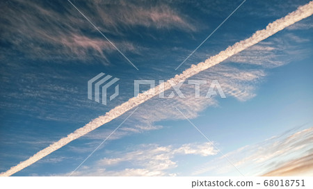 Pattern of airplane trails cutting blue sky in half. Airplane leaving behind a long white trail at the clear blue sky. 68018751