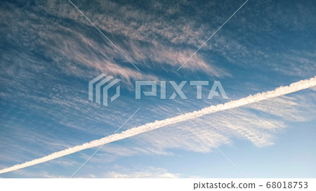 Pattern of airplane trails cutting blue sky in half. Airplane leaving behind a long white trail at the clear blue sky. 68018753