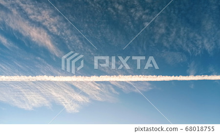 Pattern of airplane trails cutting blue sky in half. Airplane leaving behind a long white trail at the clear blue sky. 68018755