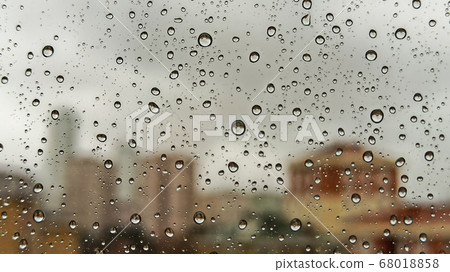 Raindrops on office window with blur grey sky background. Office window covered with closeup rain water. Raindrops on office window with blur grey sky background. Office window covered with closeup rain water. 68018858