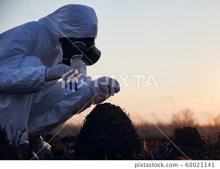 Researcher in protective suit working on a burnt field taking samples of flora 68021141