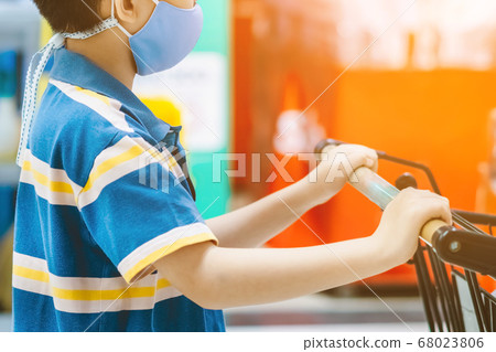 A boy wearing face mask to prevent the spread of the Corona Virus (Covid-19) shopping in a supermarket. Boy with shopping cart during virus outbreak in grocery store. New normal lifestyle. 68023806