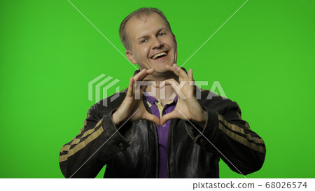 Brutal rocker man taking out heart gesture from his jacket and demonstrating romantic emotions 68026574