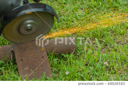cutting metal on grass with a hand tool. sparks flying from iron. selective focus. 68026583
