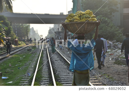 孟加拉國首都達卡，一名男子沿著不斷發展的城市景觀和鐵軌行走，頭上扛著香蕉 68029032