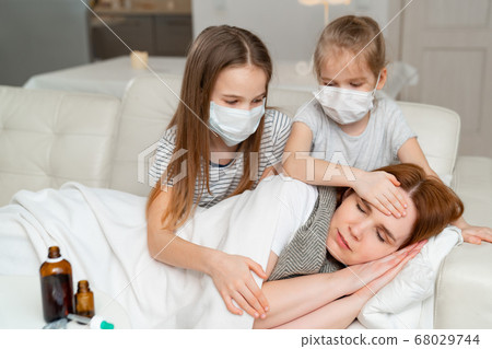 kids in masks take temperature of sick mother. 68029744