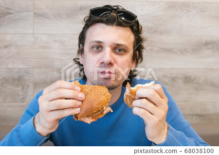 Man eating a hotdog and shawarma simultaneously sitting in cafe. 68038100